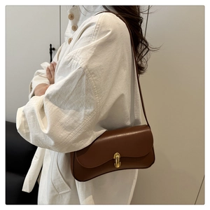 Close-up of brown leather underarm bag with gold twist lock and fine texture on shoulder