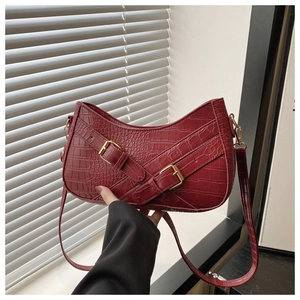 Detail of red faux crocodile leather shoulder bag with gold hardware and curved shape