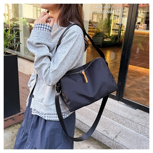 Detailed view of black nylon shoulder bag with orange leather puller and silver zipper