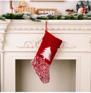 Knitted red Christmas stocking with white tree pattern hanging on a white mantel