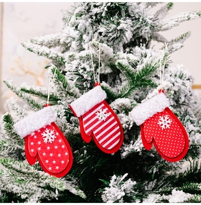 Drei rote Weihnachtshandschuh-Anhänger mit weißen Schneeflocken an grünen Zweigen