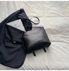 Detail einer minimalistischen schwarzen Ledertasche mit Zierbändern auf weißem Hintergrund