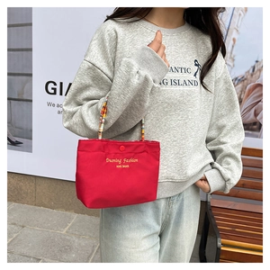 Detail of red canvas tote bag with contrast beaded handle and gold brand embroidery