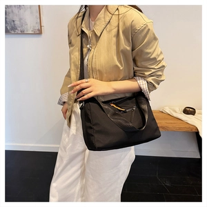 Close-up of black nylon crossbody bag with distinctive orange zipper pull detail