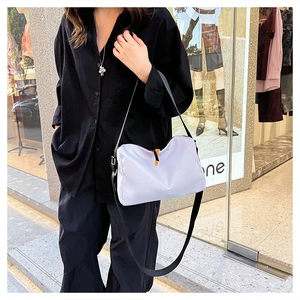 Detailed shot of a light gray nylon crossbody bag with an orange zipper accent outdoors