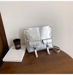 Detail der silbernen Metallic-Tasche mit Vordertaschen und Schnallen auf Holztisch