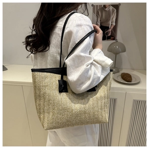 Detail of woven straw tote bag featuring black leather handles and textured natural fiber