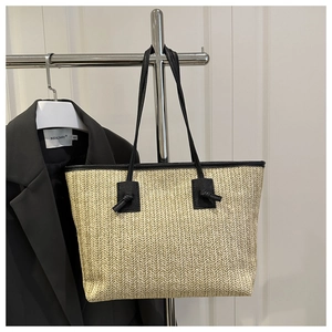 Detail of woven straw tote bag with black leather straps and V-shaped weaving texture