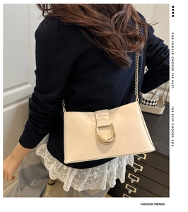 Detail of cream rectangle underarm bag featuring a gold horseshoe clasp and chain strap