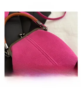 Detailed close-up of rose red canvas bag with bronze metal clasp and brown handle