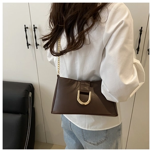 Close-up of a dark brown underarm bag featuring a U-shaped gold buckle and a fine chain strap