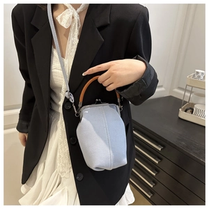 Detail of light blue canvas kiss-lock bag with brown handle worn by a model