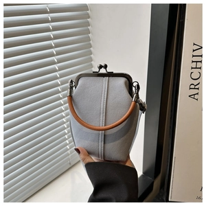 Detail of light blue fabric crossbody bag with metal clasp and brown top handle