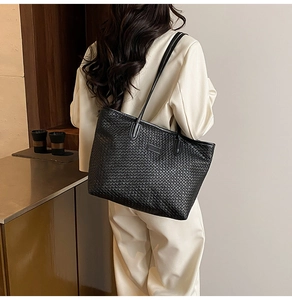 Detail of black woven leather tote bag showing texture and shoulder strap on model