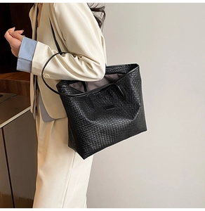 Detail of black woven tote bag with dual handles and long shoulder strap on model