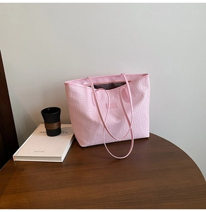 Detail of pink woven tote bag with geometric texture on a dark wood table