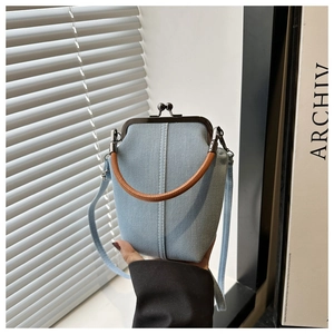 Detail of light blue kiss-lock mini bag with brown leather handle on a window sill