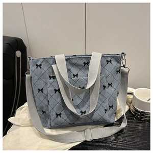 Dettaglio di un'elegante borsa tote in velluto a coste blu con fiocchi neri e manici grigi