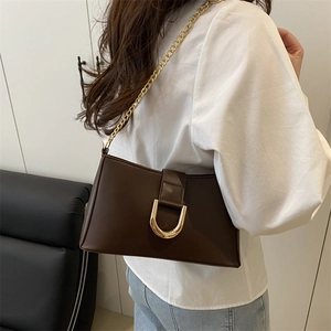 Classic dark brown leather underarm bag with gold metal buckle and chain strap on a model