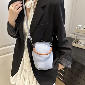 Vertical light blue denim crossbody bag with leather handle and kiss-lock closure on model