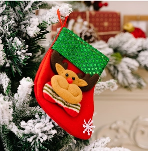 Detail of Christmas stocking with green sequins and plush reindeer on a snowy tree