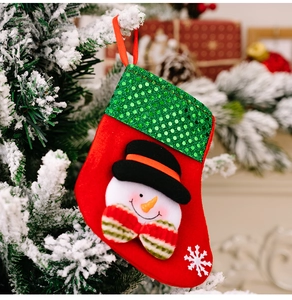 Detail of Christmas stocking with green sequins and snowman hanging on a snowy tree branch