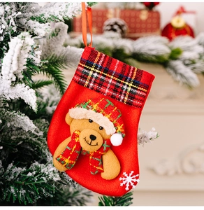 Detail of red Christmas stocking with plaid trim and 3D bear hanging on a snowy tree