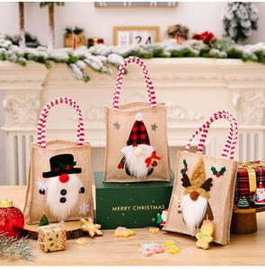 Three Christmas burlap gift bags with gnome embroidery and red striped handles on a table