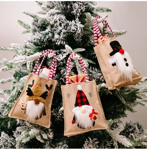 Detailed view of three hanging burlap Christmas gnome gift bags on snowy tree branches