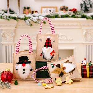 Set of 3 burlap Christmas gnome gift bags with red striped handles on wooden table