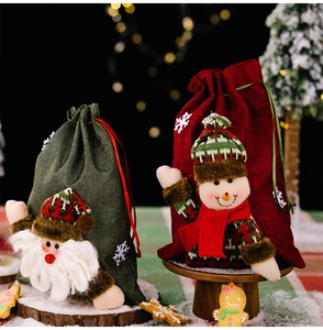Linen Christmas gift bags with plush Santa and Snowman figures on snowy wooden base