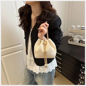 Detail of cream woven bucket bag with gold chain strap and pearl drawstring charms