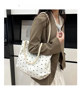 Detail of white bucket bag featuring black bow embroidery and woven rope handles