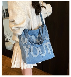 Detail of blue denim tote bag with ONLY YOU lettering and distressed frayed edges