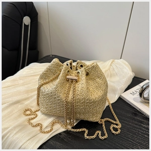 Détail d'un sac seau en paille tressée avec chaîne dorée et cordon en perles chic