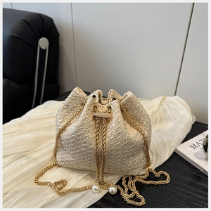 Détail du sac seau en paille beige avec chaîne dorée et élégants accents de perles