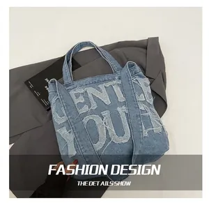 Detail of blue denim tote bag with frayed letter patchwork and wide shoulder strap