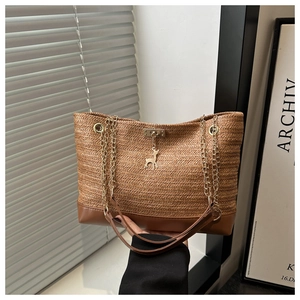Close-up of woven straw tote bag featuring a gold deer charm and chain shoulder strap