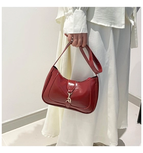 Close-up of deep red glossy saddle bag with golden metal hook clasp held by model