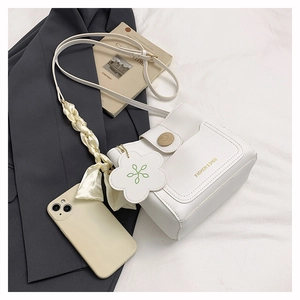Détail d'un sac bandoulière blanc avec bouton en bois et breloque fleurie chic