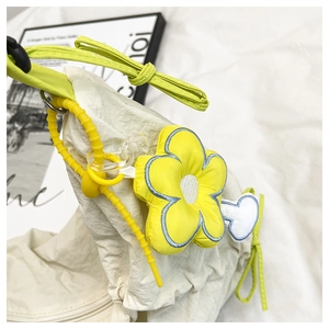 Détail du sac beige en toile avec bandoulières jaune néon et accessoire fleur suspendu