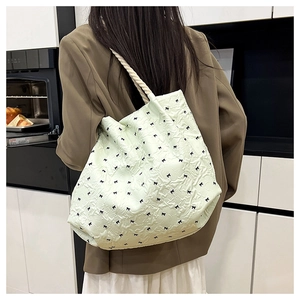 Model wearing a light green textured tote bag with black bow embroidery and rope straps