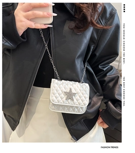 Detail of white quilted crossbody bag featuring a silver rhinestone star and chain strap