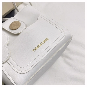 Détail du sac à main en cuir blanc grainé avec bouton en bois et logo doré élégant