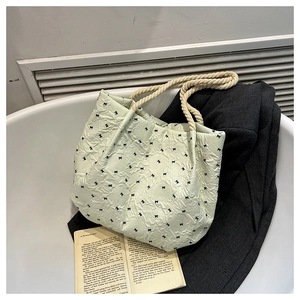 Detail of light green bucket bag with bubble texture and black bow print by a white bathtub