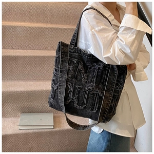 Close-up of black washed denim tote bag featuring raw-edge letter applique and wide strap