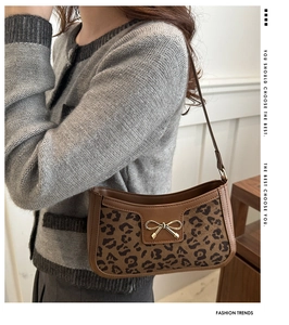 Detail of leopard print baguette bag with golden bow buckle and brown leather trim