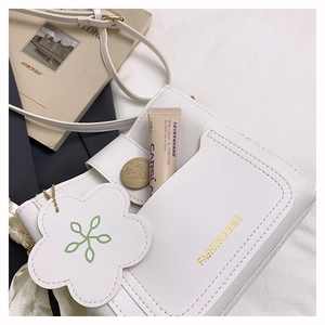 Détail d'un sac en cuir blanc avec lettrage doré et pendentif fleur chic
