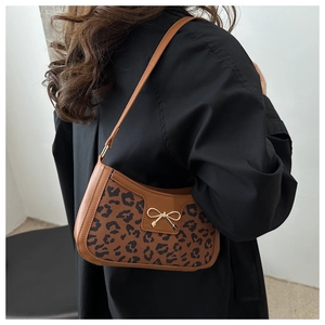 Close-up of leopard print underarm bag featuring a gold metal bow and brown trim