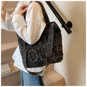 Detail of black vintage washed denim tote bag with oversized letter patches and frayed edges